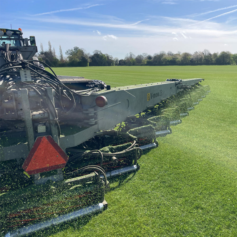 Premium grade turf being cut by machinery being towed by a tractor on a sunny day.