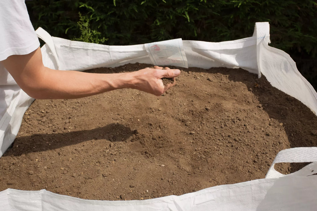 a person with a handful of topsoil from a ton bag after delivery 